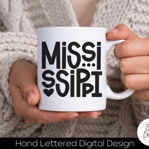 May include: White ceramic mug with a black hand-lettered design that says "MISSISSIPPI" with a heart in the middle of the word "MISSI".