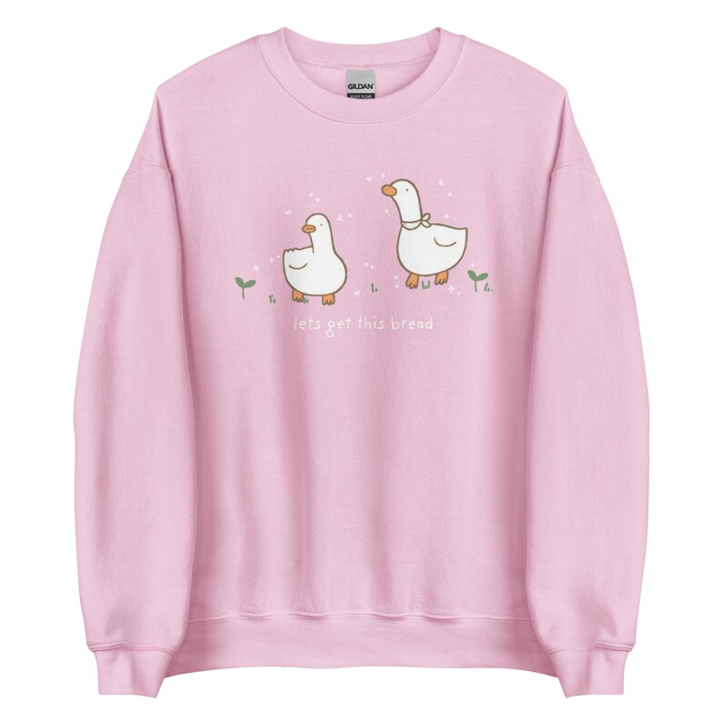 Pastel Pink Whimsical Duck Sweatshirt with a dtg printed design of two ducks surrounded by sparkles, and below it says " lets get this bread"