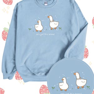 May include: Light blue sweatshirt with a graphic of two white geese and the text "lets get this bread".