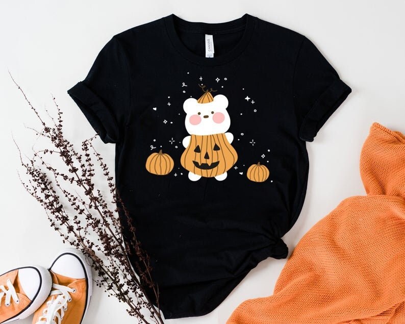Op de afbeelding: Zwart T-shirt met een witte beer die een pompoenkostuum draagt. De beer heeft een schattig gezicht en is omringd door kleine pompoenen. Het shirt heeft een Halloween-thema.