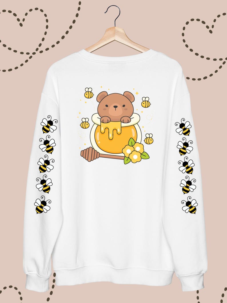 Puede incluir: Sudadera blanca con un oso de dibujos animados en un tarro de miel en la espalda. Las mangas tienen un patr&oacute;n repetitivo de abejas de dibujos animados.