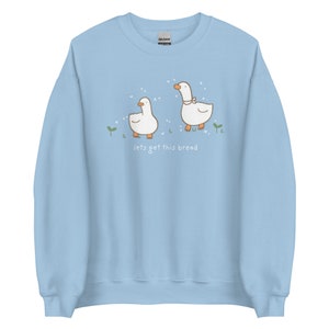 Pastel Blue Whimsical Duck Sweatshirt with a dtg printed design of two ducks surrounded by sparkles, and below it says " lets get this bread"