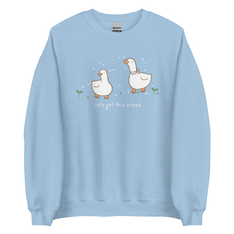 Pastel Blue Whimsical Duck Sweatshirt with a dtg printed design of two ducks surrounded by sparkles, and below it says " lets get this bread"