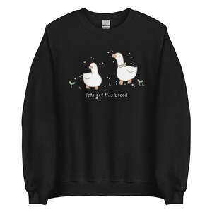 black Whimsical Duck Sweatshirt with a dtg printed design of two ducks surrounded by sparkles, and below it says " lets get this bread"