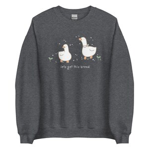 Dark grey Whimsical Duck Sweatshirt with a dtg printed design of two ducks surrounded by sparkles, and below it says " lets get this bread"