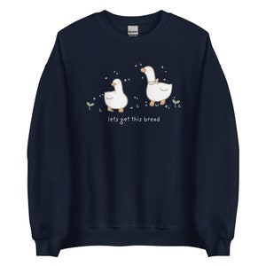 navy Blue Whimsical Duck Sweatshirt with a dtg printed design of two ducks surrounded by sparkles, and below it says " lets get this bread"