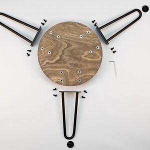 May include: A set of three black metal hairpin legs for a table or chair, with a round wooden tabletop. The legs are attached to the tabletop with screws.