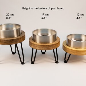 May include: Three stainless steel pet bowls on wooden stands with black metal legs. The bowls are 22 cm, 17 cm, and 12 cm tall.
