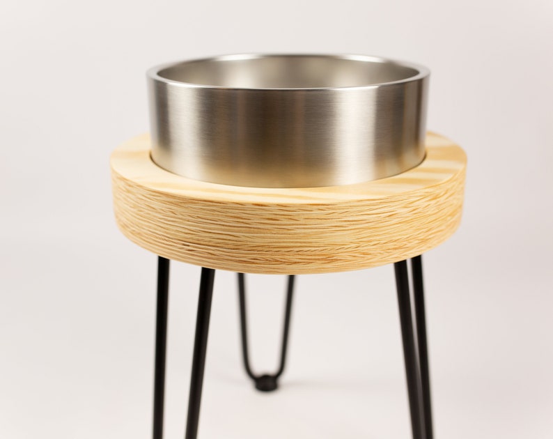 May include: A wooden plant stand with a metal planter. The stand has three black metal legs and a round wooden top. The planter is made of stainless steel and has a smooth, shiny finish.