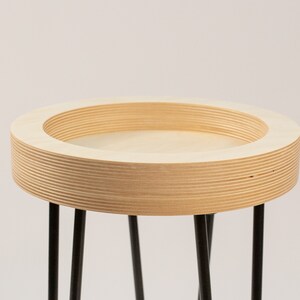 May include: A round wooden table with a black metal base. The table top is made of plywood and has a natural wood finish.