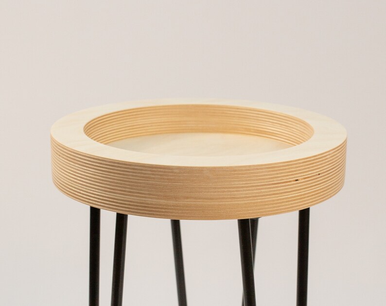 May include: A round wooden table with a black metal base. The table top is made of plywood and has a natural wood finish.