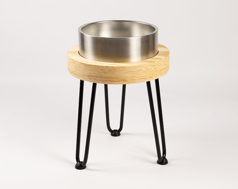 May include: A stainless steel pet bowl raised on a wooden platform with black hairpin legs.