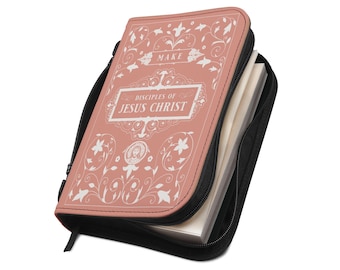 Puede incluir: Una funda de libro de color rosa empolvado con cierre de cremallera negro. La parte frontal presenta motivos florales blancos y el texto "MAKE DISCIPLES OF JESUS CHRIST" en un marco rectangular, con un pequeño icono circular que muestra un rostro.