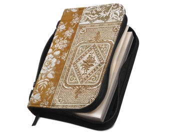 Puede incluir: Una funda para libro con cremallera que presenta un panel amarillo mostaza con un patrón floral blanco junto a un panel central que muestra un intrincado diseño de damasco beige y blanco con un motivo floral en forma de diamante, conteniendo papel.
