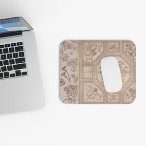 May include: A rectangular mouse pad featuring a split design with a botanical illustration of flowers on the left and an intricate, beige-toned architectural ceiling pattern on the right, with a plain white computer mouse resting on top.
