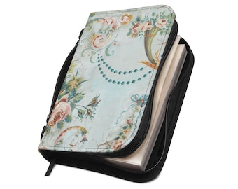 Puede incluir: Una funda para libro con cremallera sobre un fondo azul claro con un patrón floral de rosas rosadas, hojas verdes y guirnaldas de cuentas color cerceta. La funda tiene un cierre de cremallera negro y borde negro, conteniendo páginas blancas.