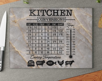 Puede incluir: Una tabla de cortar rectangular de vidrio con un patrón de mármol gris claro y vetas doradas. La superficie presenta una tabla de conversión de cocina impresa en negro, una escala de temperatura y varios iconos de cocción.