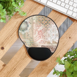 Könnte beinhalten: Ein rundes Mauspad mit einem Vintage-Blumenmuster und einer schwarzen Handgelenkauflage. Das Design zeigt einen Patchwork aus Blumenmustern, handschriftlichem Text und geometrischen Formen in Creme-, Rosa-, Blau- und Brauntönen.