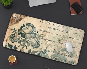Puede incluir: Una alfombrilla de escritorio rectangular con un diseño de inspiración vintage que presenta una gran ilustración floral de color verde azulado oscuro sobre un fondo crema que recuerda a papel de registro envejecido con texto escrito.