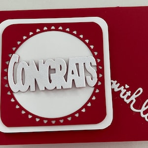 May include: A red card with a white square and circle cutout. The circle has a white "CONGRATS" with a heart border. The card says "with love" in white cursive.