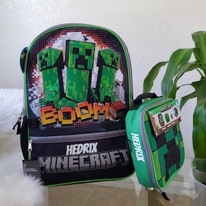 May include: A black and green Hedrix Minecraft backpack and matching lunch bag. The backpack features green pixelated Creeper characters with the word "BOOM" and a TNT block. The lunch bag has a green and black Creeper design.