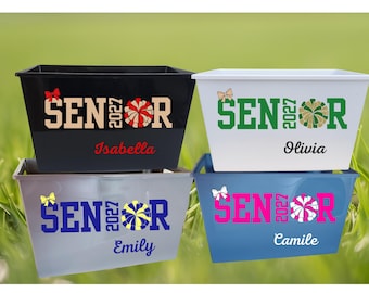 May include: Four rectangular plastic storage bins in black, white, grey, and blue. Each bin features the text SENIOR 2027 with a pom-pom graphic replacing the letter O, a small bow icon, and a personalised name printed in a script font.