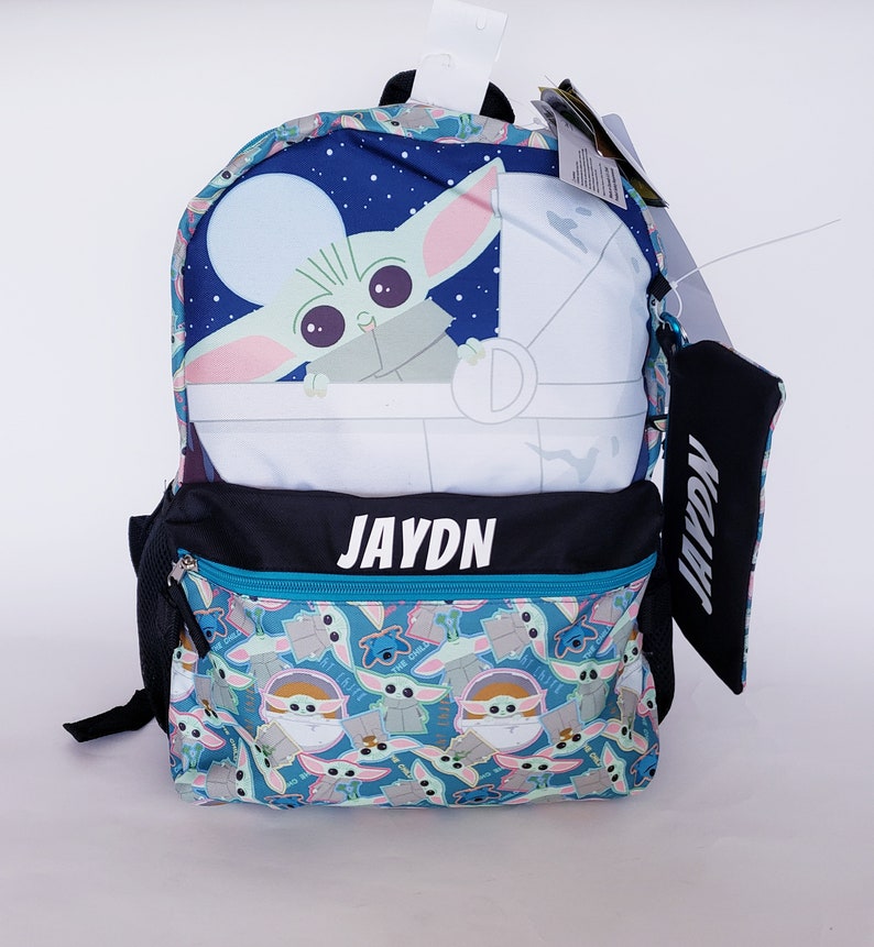 Pode incluir: Uma mochila azul com um design de Grogu de The Mandalorian. O painel superior mostra Grogu numa cena espacial. O bolso frontal tem um padr&atilde;o de Grogu e Stitch. O nome "JAYDN" est&aacute; impresso em branco na frente.