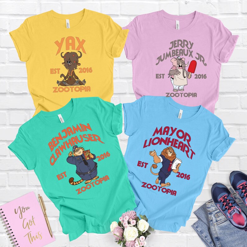 a collection of four colorful t-shirts, each with a unique design and text, arranged on a white brick wall.