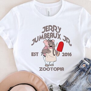 A white t-shirt with a graphic design featuring an elephant holding a red popsicle, along with text that reads "JERRY JUMBEAUX JR EST 2016 Zootopia".