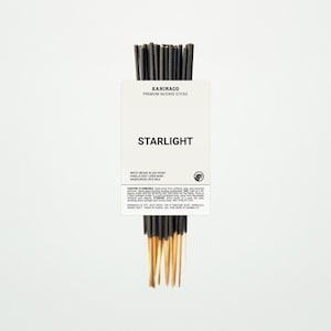 May include: A collection of incense sticks with gold-coloured tips and a white label. The label displays "KANIMACO PREMIUM INCENSE STICKS" and "STARLIGHT". The fragrance includes white orchid, blush peony, vanilla dust, linen musk, sandalwood, and rice milk.