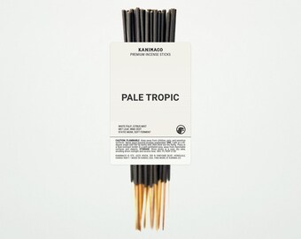 May include: A bundle of KANIMACO premium incense sticks. The sticks are black with gold tips, and are wrapped with a white label that reads "PALE TROPIC". The label also lists the scent notes: white pulp, citrus mist, wet leaf, ring zest, static musk, and soft ferment.
