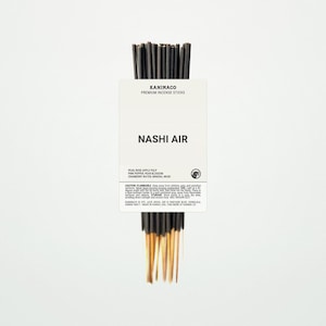 May include: A bundle of black incense sticks with gold tips, held together by a white label. The label reads "KANIMACO PREMIUM INCENSE STICKS" and "NASHI AIR". The scent includes pear, rose, apple, pink pepper, cranberry, and mineral musk.