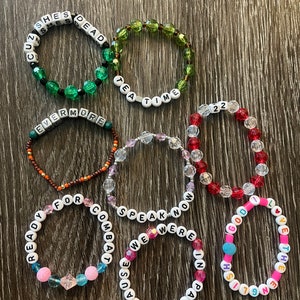 May include: Seven beaded bracelets with different coloured beads and white letter beads spelling out phrases like "She's Dead", "Tea Time", "Evermore", "Ready For Combat", "Speak Now", "We Were In Paris", and "1991 English God I Love The End".