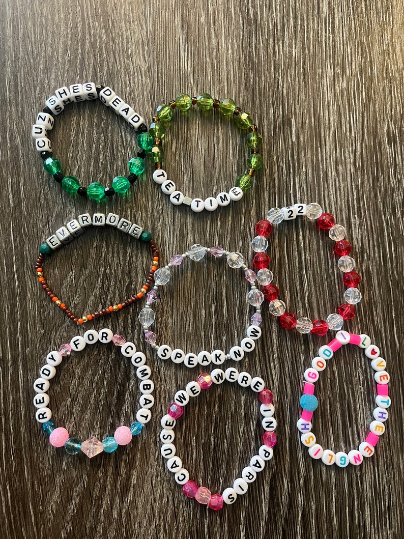 May include: Seven beaded bracelets with different coloured beads and white letter beads spelling out phrases like "She's Dead", "Tea Time", "Evermore", "Ready For Combat", "Speak Now", "We Were In Paris", and "1991 English God I Love The End".