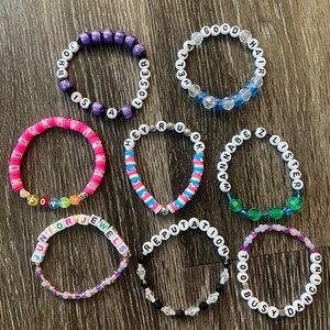 May include: Ten colourful beaded bracelets with different song titles and lyrics from the singer Taylor Swift. The bracelets are made with white letter beads and colourful beads.