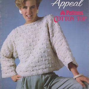 May include: A woman models a cream-coloured, textured cotton top with long sleeves and a boat neck. The top is part of a knitting and crochet pattern titled "Sun Appeal" by Susan Bates. The image also shows light green trousers.