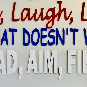 May include: A white background with the phrases "Live, Laugh, Love" in red, "IF THAT DOESN'T WORK" in blue, and "LOAD, AIM, FIRE!" in white. The words are in a bold, sans-serif font.