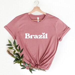 May include: A dusty rose t-shirt with a white graphic that says "Brazil" with a small heart above the "z".