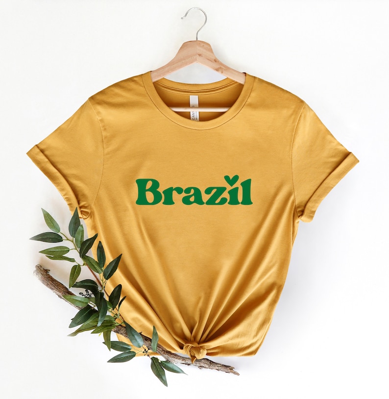 May include: A mustard yellow t-shirt with a green graphic that says "Brazil" with a small heart above the "z".
