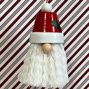 May include: A white yarn beard gnome ornament with a red and white Santa hat with a green holly sprig.