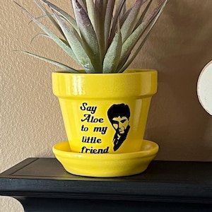 May include: Yellow ceramic planter with a black silhouette of a man and the text "Say Aloe to my little friend".