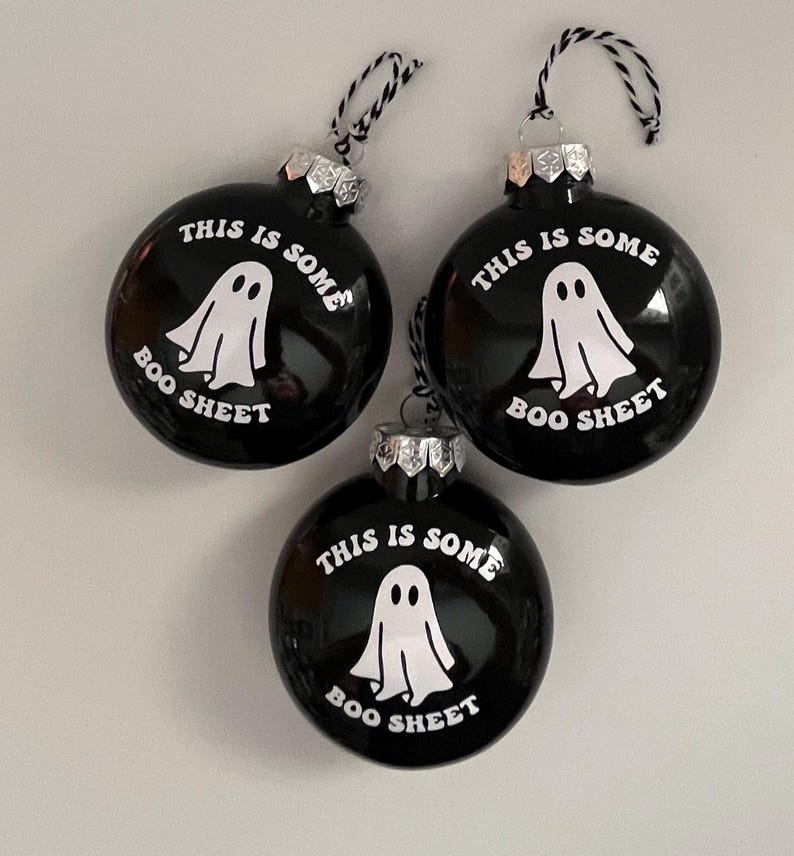 May include: Three black Christmas ornaments with the text "THIS IS SOME BOO SHEET" and a white ghost graphic. Each ornament has a silver cap and a black and white string for hanging. The ornaments are round and glossy.