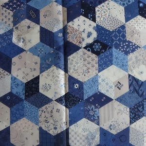 May include: A fabric with a geometric pattern of blue and white hexagons. The design creates a 3D cube effect, with each hexagon featuring a different floral or patterned design. The color palette includes shades of blue and white.