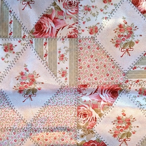 Puede incluir: Una tela de patchwork con fondo blanco y un patrón repetido de rosas rosas y rojas. La tela está cosida en forma de diamante con un hilo marrón claro.