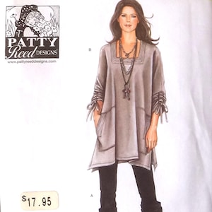 Puede incluir: Un sobre de patrón de costura Simplicity 1543 A de Patty Reed Designs con un dibujo lineal de una túnica con escote cuadrado, bolsillos laterales y lazos en las mangas. El patrón cubre las tallas XXS-XXL. La ilustración muestra una túnica gris combinada con leggings negros y botas, con collares superpuestos.