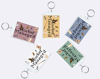 May include: Four keychains with clear plastic frames and silver key rings. Each keychain features a different colored background with a witch's hat, a wand, a book, and a mug. The text on each keychain reads "Mischief Managed".