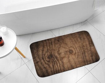 Könnte beinhalten: Eine braune Badezimmermatte in Holzoptik mit strukturierter Oberfläche. Die Matte liegt auf einem weißen Fliesenboden in einem Badezimmer.