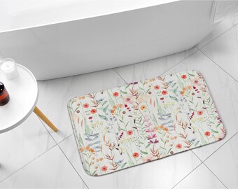 May include: A white bath mat with a floral pattern featuring watercolor-style flowers in shades of pink, red, orange, and yellow. The flowers are arranged in a random pattern on a white background.
