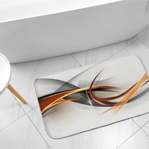 May include: Abstract bath mat with orange, yellow, and gray swirling lines on a white background.