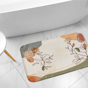 May include: A beige bath mat with an abstract floral design in shades of brown, orange, and green. The design features stylized flowers and leaves with a geometric pattern.